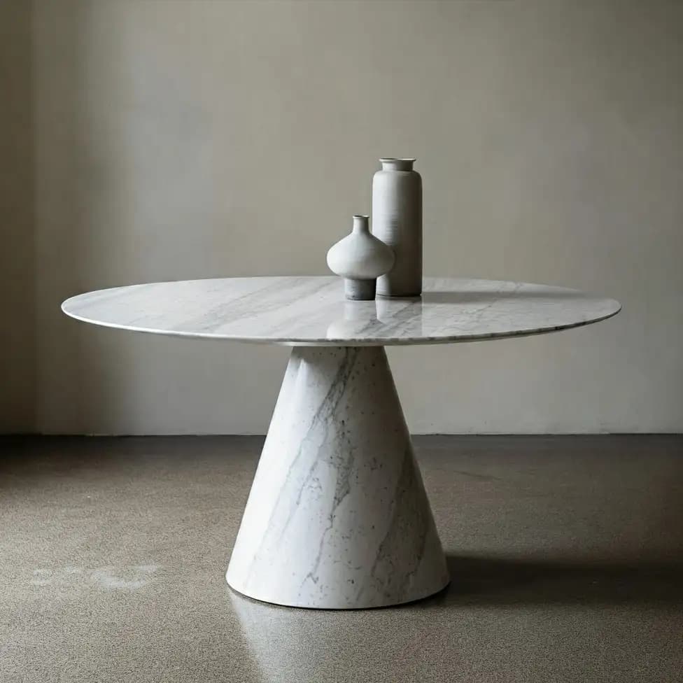 A round marble dining table balanced on a single conical marble pedestal